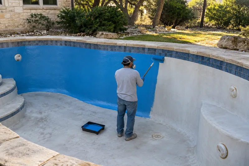 Blue epoxy pool paint being rolled onto a drained pool wall
