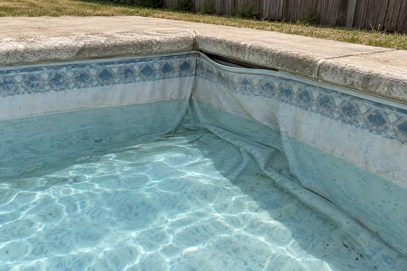 Faded, wrinkled vinyl pool liner pulling out of its track