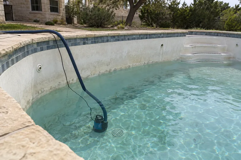 Submersible pump draining a pool through a hose over the coping