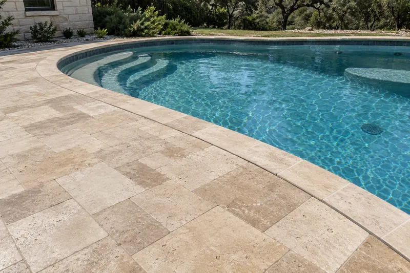 Tumbled travertine paver deck with a sealed joint at the pool coping