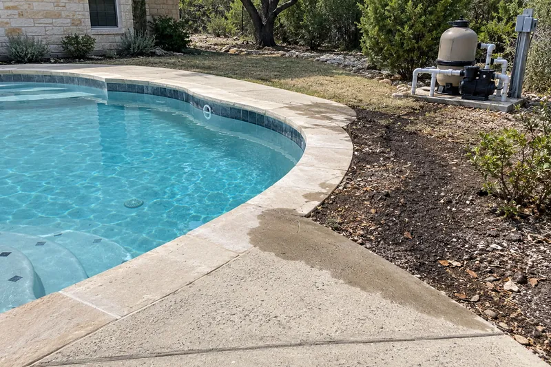 Wet ground along a pool's plumbing run beside the deck